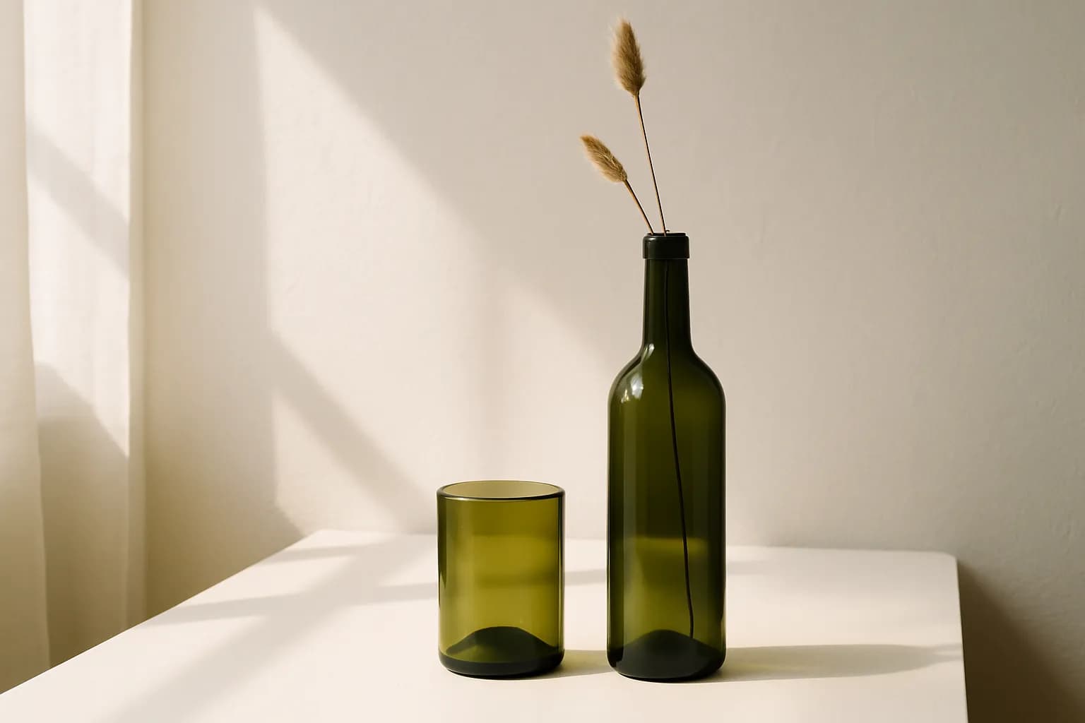 A cut wine bottle sanded into a smooth-rimmed tumbler beside a whole bottle holding a single dried stem